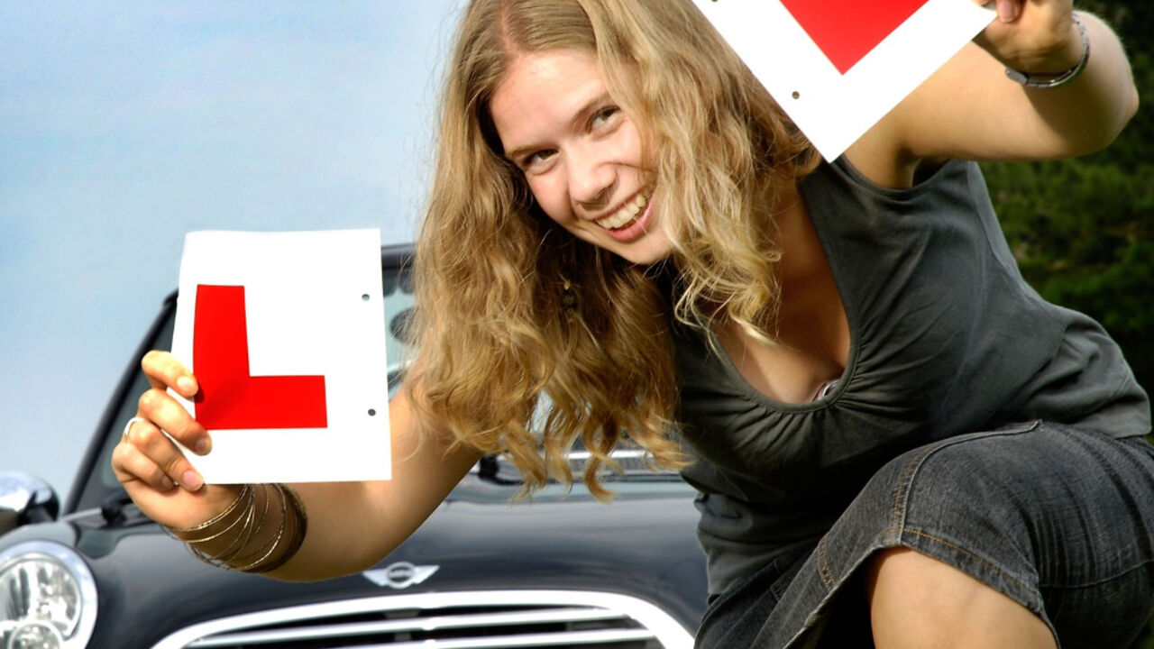 devojka čuči ispred auta sa L znakom